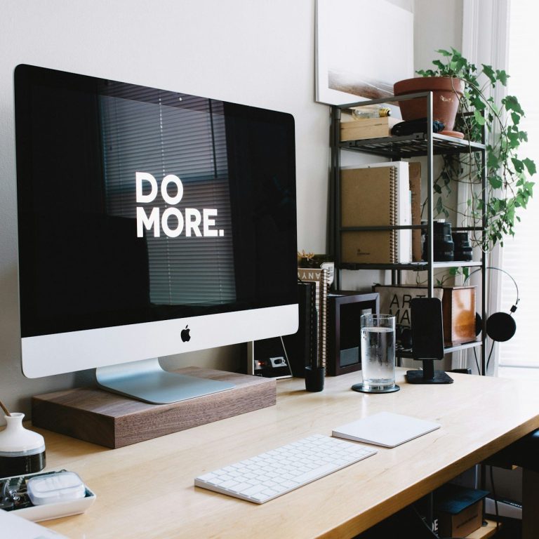 Bureau moderne avec un ordinateur affichant "DO MORE" et des plantes décoratives.